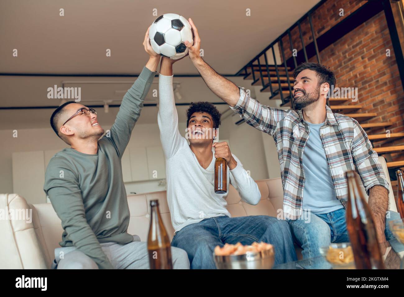 Three joyous friends lifting a soccer ball together Stock Photo Alamy