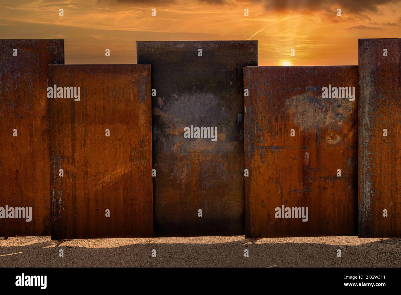 A composite of an fence made of rusty steel slabs and a glowing sunset Stock Photo