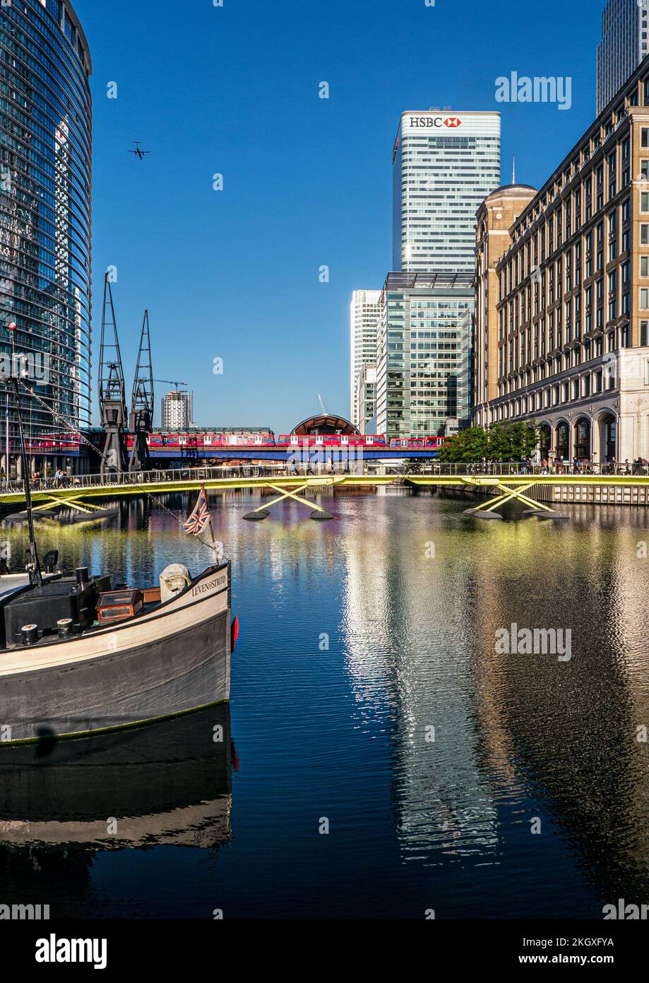 Canary Wharf at West India Docks with barge in foreground & HSBC building. West India Quay DLR Crossrail tube rail station behind London E14 Stock Photo