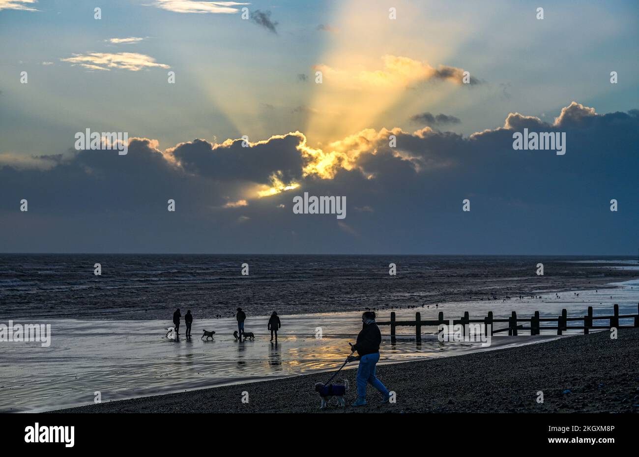 Worthing UK 23rd November 2022 - The sun hides behind dark clouds as dog walkers enjoy a late afternoon stroll along Lancing beach at low tide after a day of sunshine and heavy showers  : Credit Simon Dack / Alamy Live News Stock Photo