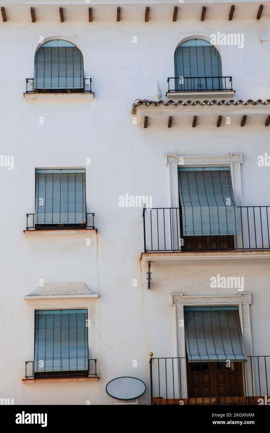 A white Spanish building with six windows all with blue blinds Stock Photo