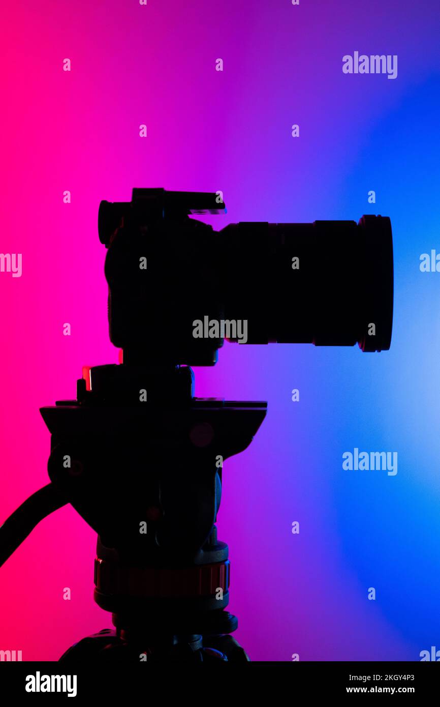 A vertical shot of a silhouette of a camera on a tripod against a blue ...
