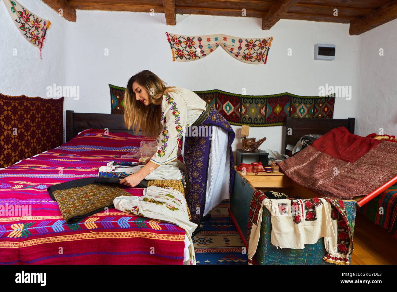 Young Romanian woman opening the wedding chest with many traditional costumes to try on Stock Photo