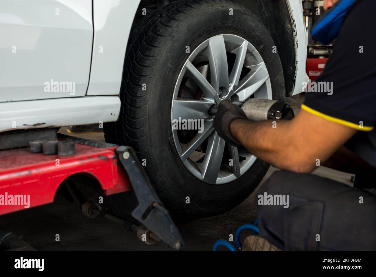 Auto mechanic man with electric screwdriver changing tire outside. Car