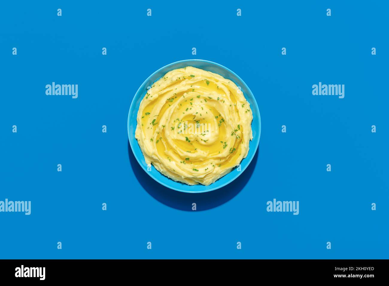 Top view with a bowl with mashed potatoes, minimalist on a blue background. Creamy mashed potatoes with olive oil and parsley. Stock Photo