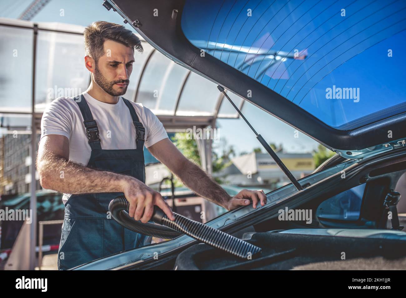 Experienced service station worker vacuuming the dirty automobile interior Stock Photo