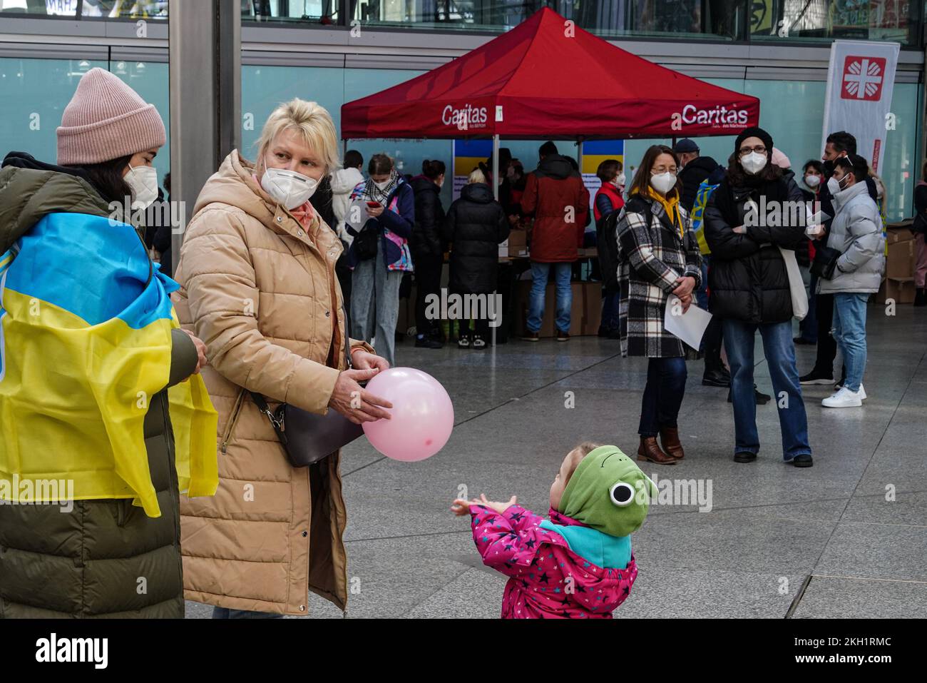 A woman from Ukraine has a balloon in her hands and is chatting with a volunteer at  station Munich. Her little granddaughter demands attention. Stock Photo