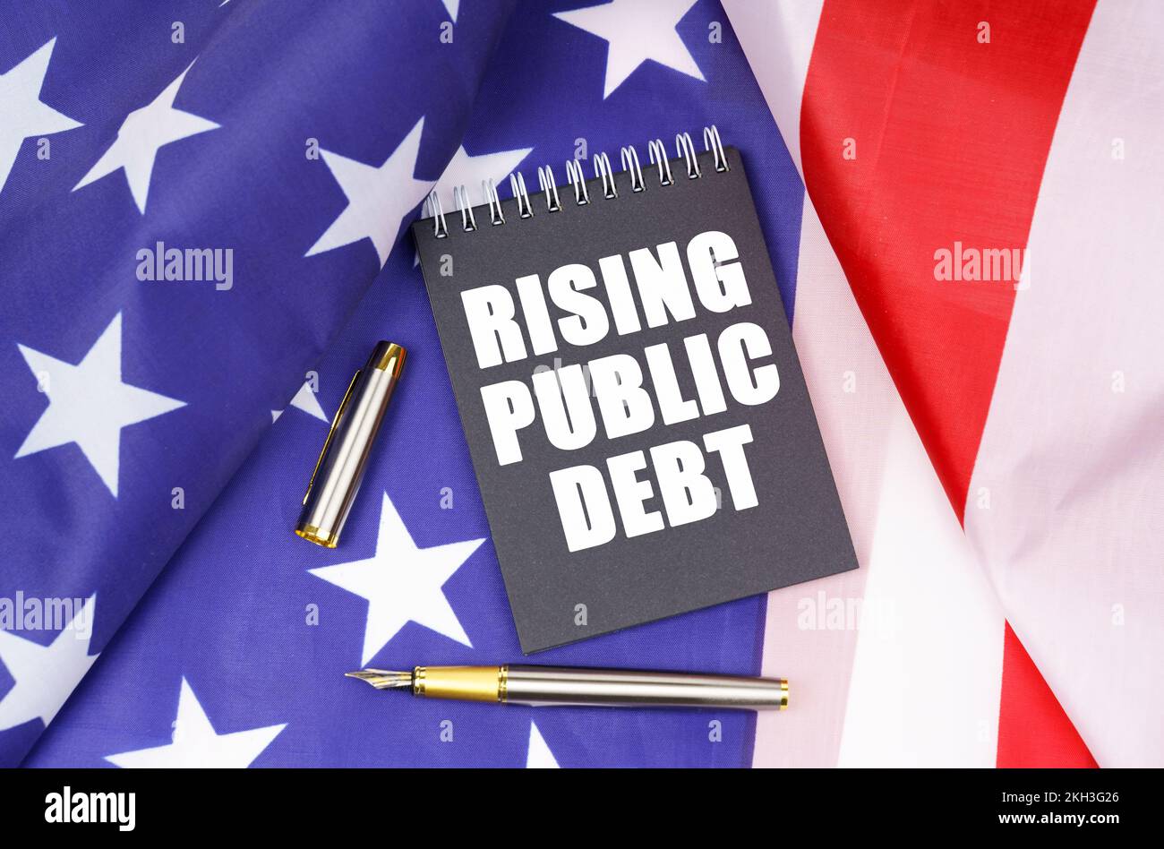 Business concept. On the American flag lies a pen and a notebook with the inscription - rising public debt Stock Photo
