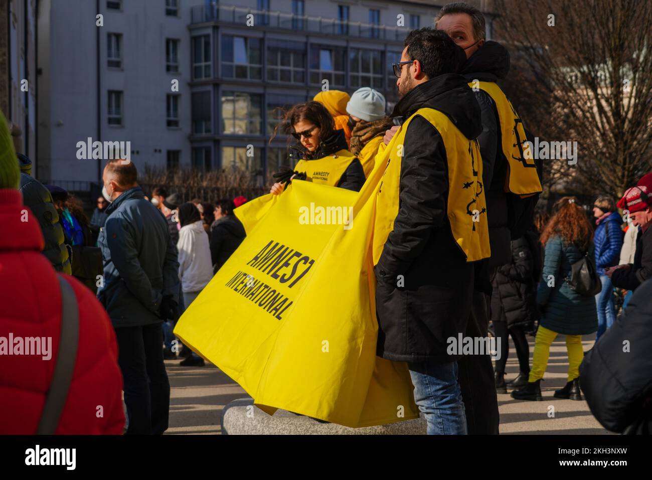 Members of Amnesty International hold a large yellow banner with their logo in front of them at a demonstration against Putin's war in Ukraine. Stock Photo