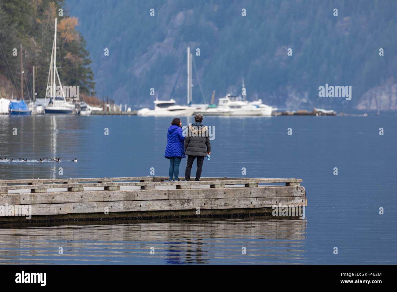 Couple dreaming on the wooden jetty at a lake on a cold autumn day. Mature couple relaxing and enjoying the beautiful view on the dock at Indian Arm V Stock Photo