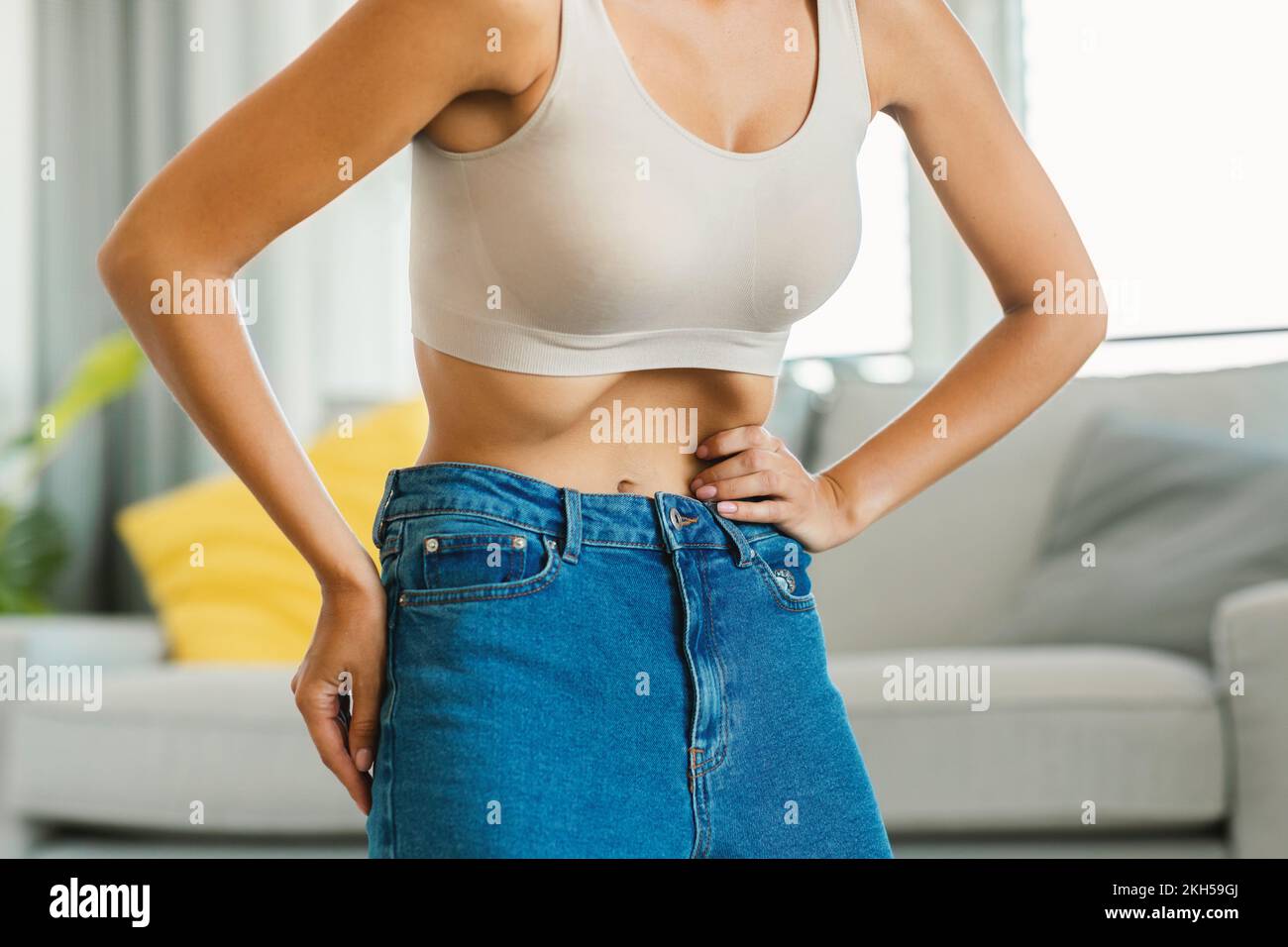 Unrecognizable young lady doing stomach vacuum exercise, flexing abdominal muscles, standing at home, closeup Stock Photo