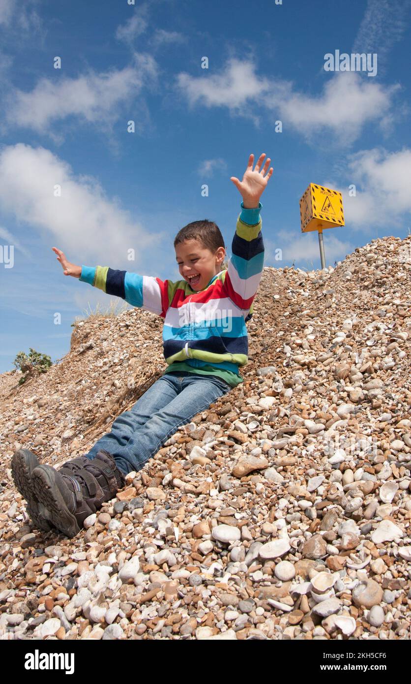 young boy sliding down hillside on beach, Pagham, West Sussex, England