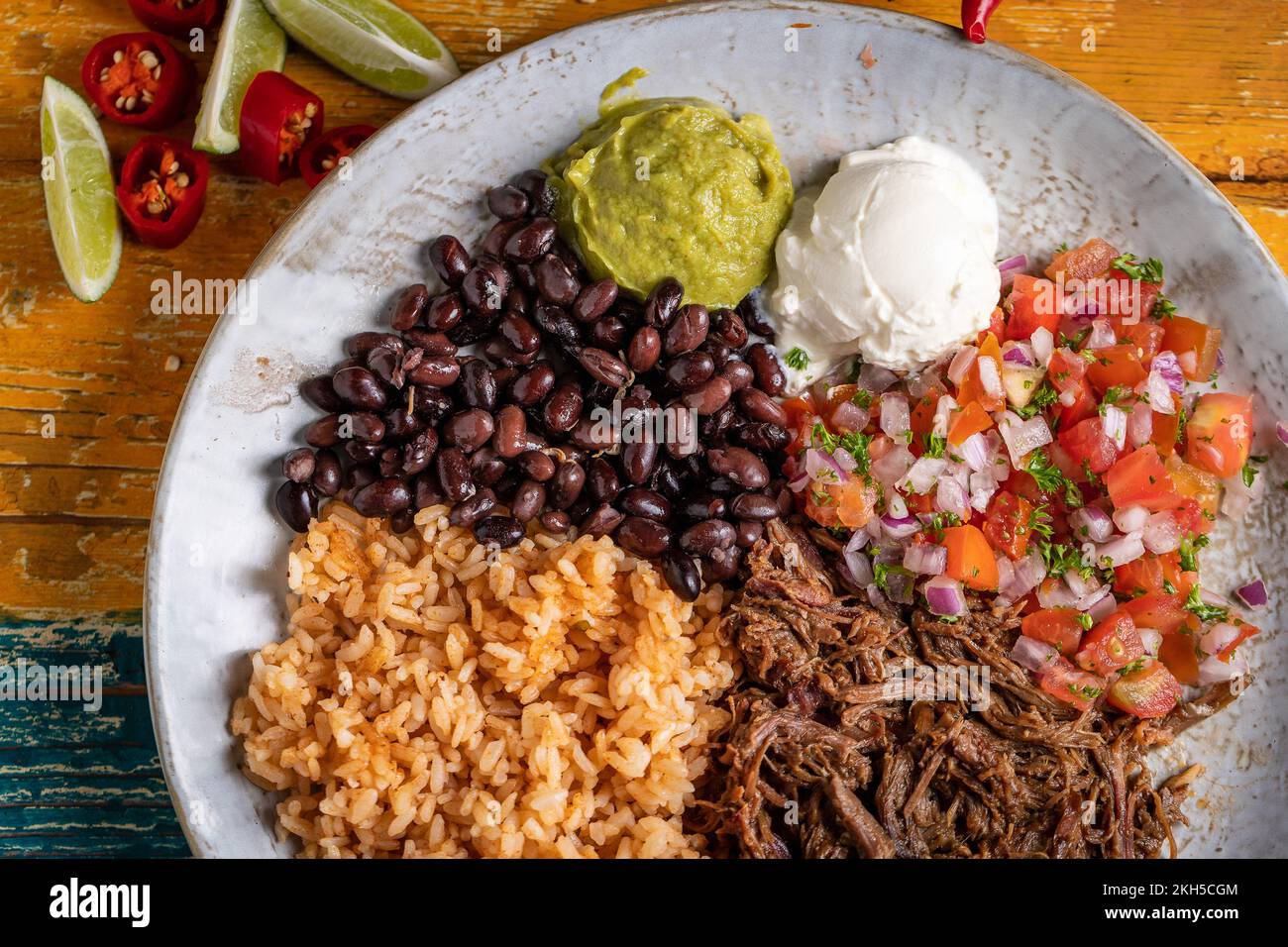 A topview of a barbacoa burrito bowl, meat rice black beans sour cream
