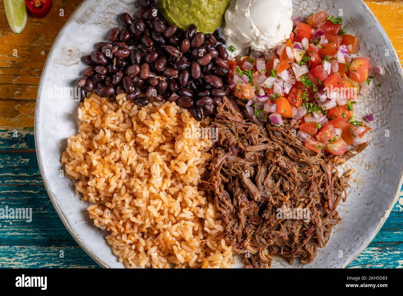 A top-view of a barbacoa burrito bowl, meat rice black beans sour cream