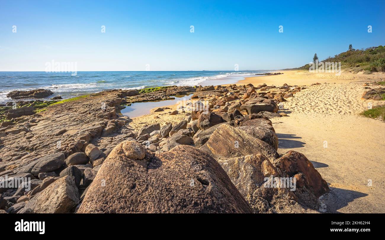 Volcanic rocky shelf with a rock pool at Point Arkwright, Coolum, Sunshine Coast, Queensland. Looking south along the sandy surf beach. Stock Photo