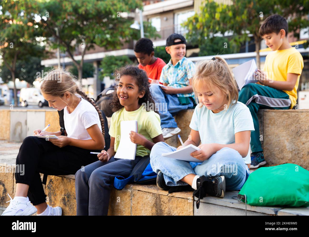 Tweenagers studying outside school, writing in workbooks Stock Photo