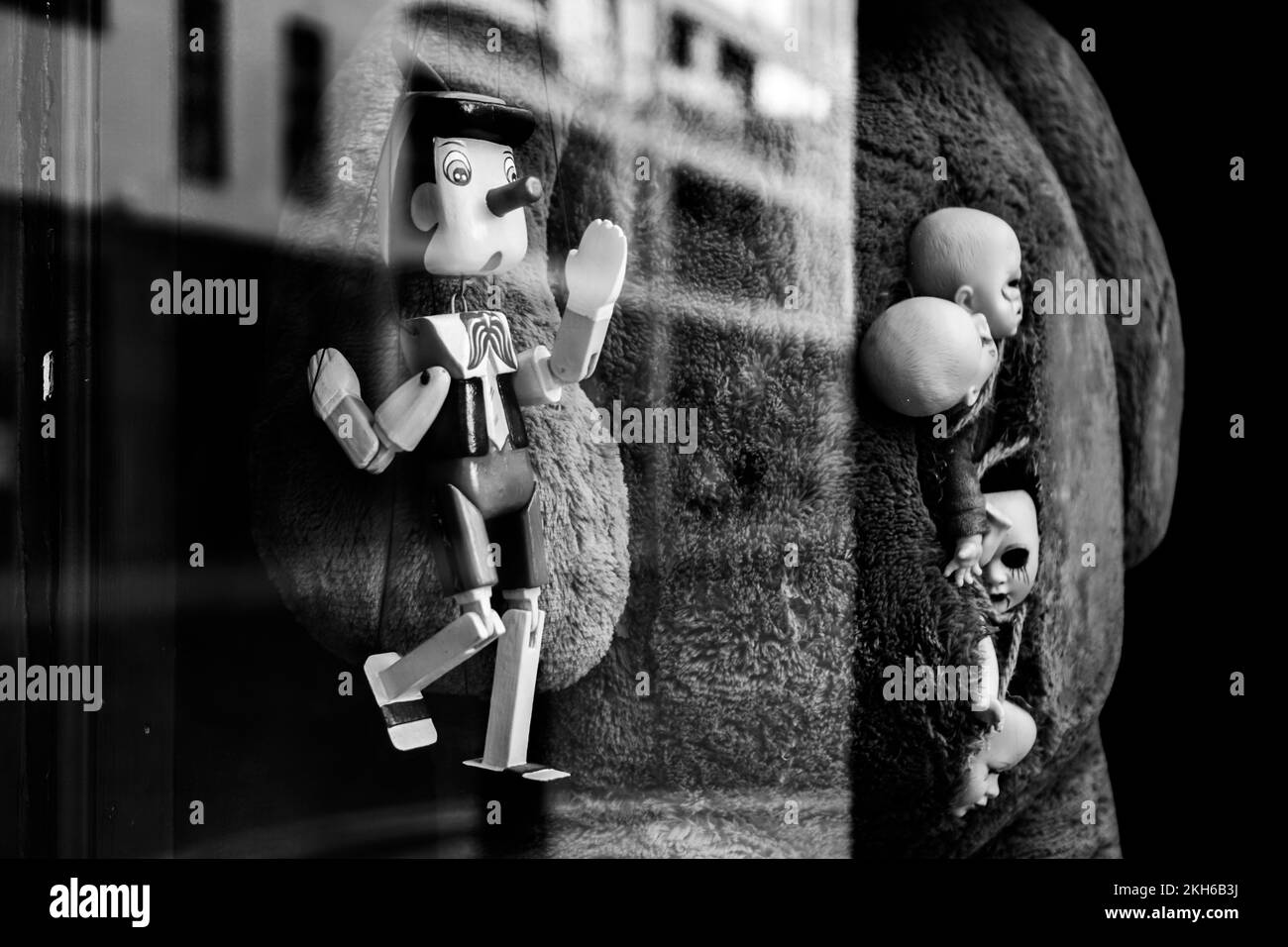 A grayscale of toys displayed in a shop window with glass reflecting the buildings outside Stock Photo