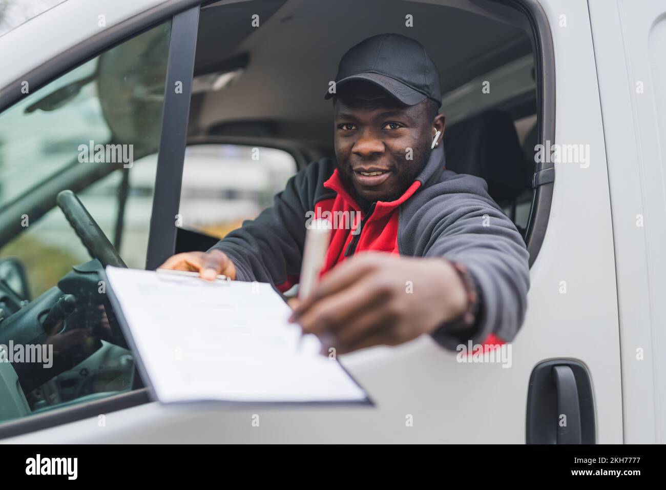 Positive AfricanAmerican deliveryman behind the wheel of white