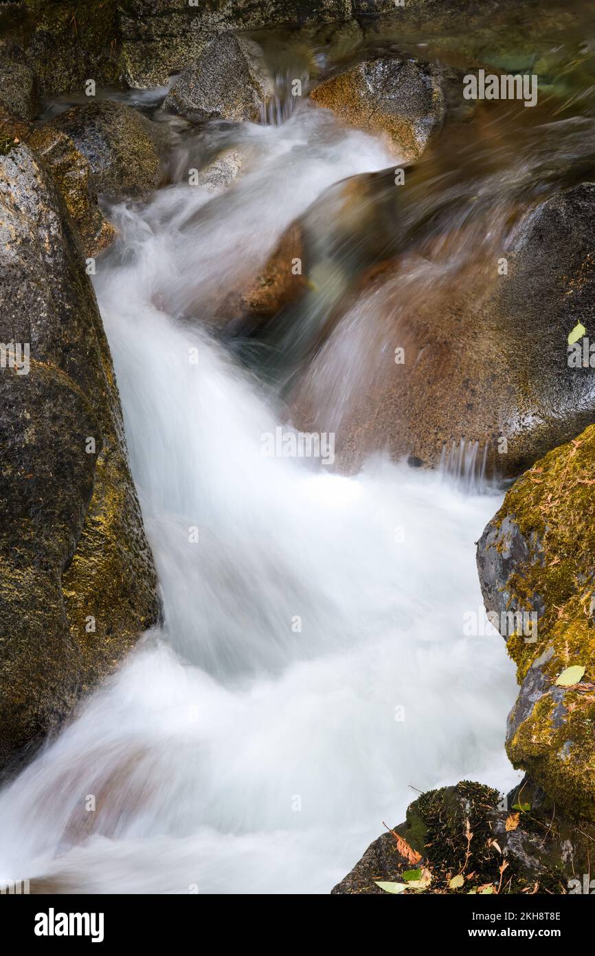 Mountain stream cascades in closeup between colorful boulders and moss with silky smooth water Stock Photo