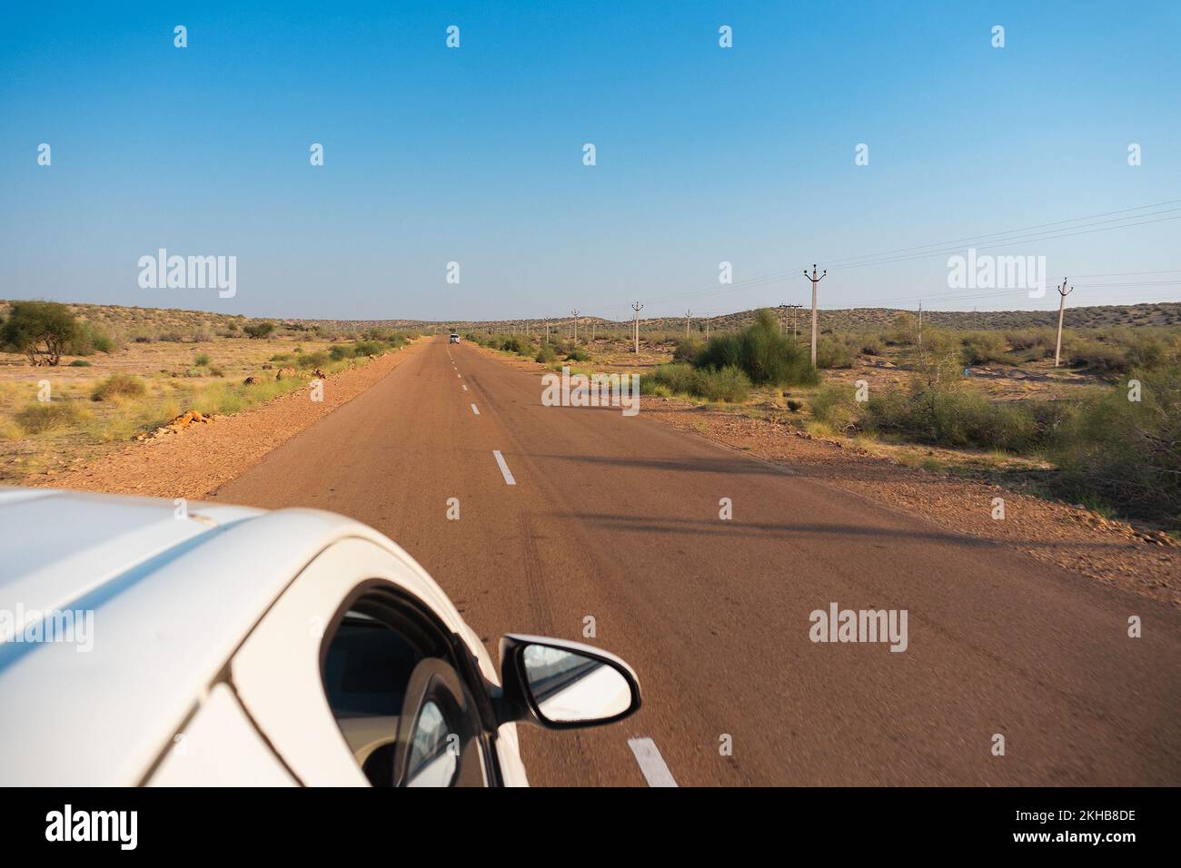 White car running through empty high road or national high way passing through the desert. Distant horizon, Hot summer at Thar desert, Rajasthan, Indi Stock Photo
