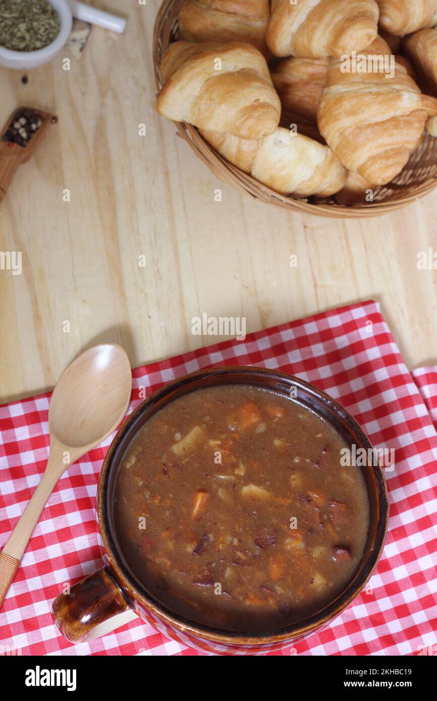 Beef Stew and Fresh Bread in Rustic Kitchen With Red and White Checkered Cloth on Wooden Table Stock Photo