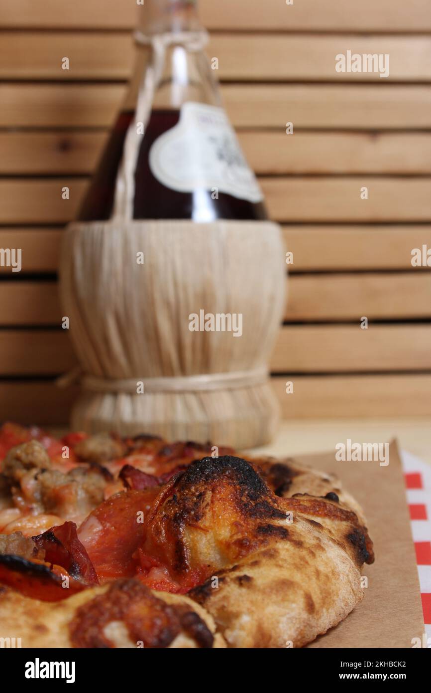 Fresh Pizza on Wooden Table at Restaurant With Bottle of Chianti Wine Stock Photo