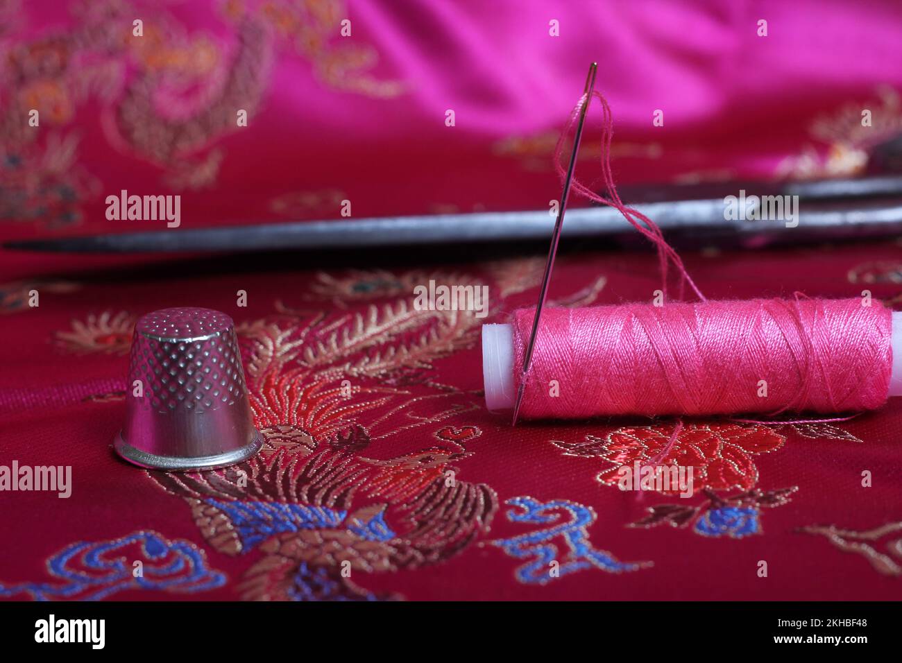 Spool of Pink Thread and Thimble on Vintage Pink Satin Stock Photo