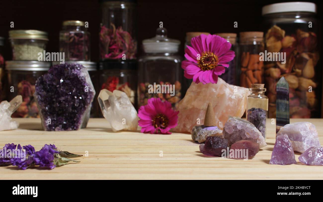 Amethyst Crystals and Flowers On Meditation Table With Jars of Dried Herbs in Background Stock Photo