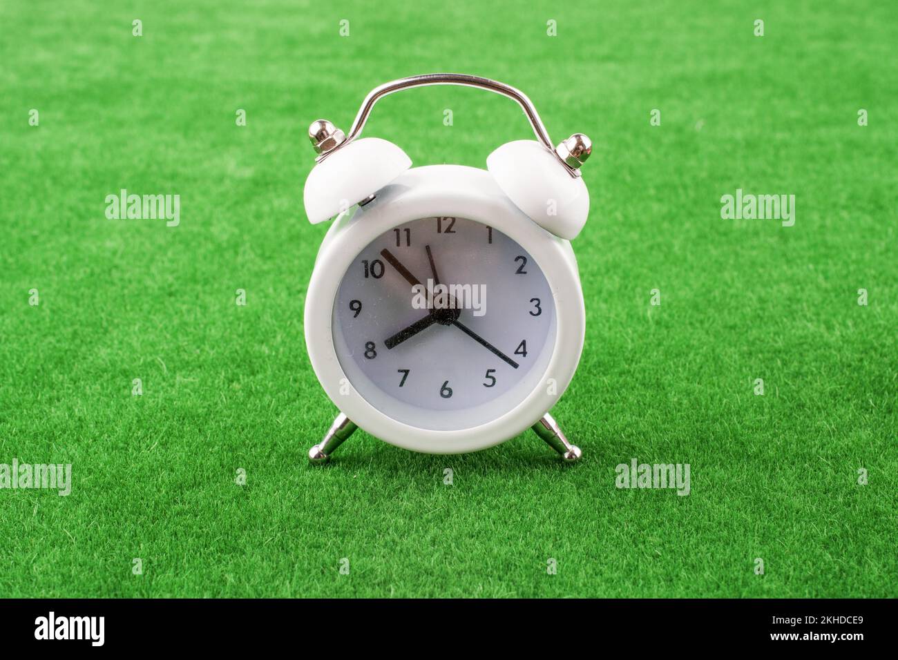 White color alarm clock a on a green grass background Stock Photo - Alamy