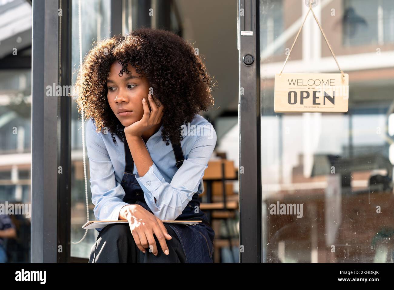 Young african female has sad mood with waiting customer in front of the door of cafe because due to viral infection. Coronavirus and quarantine Stock Photo