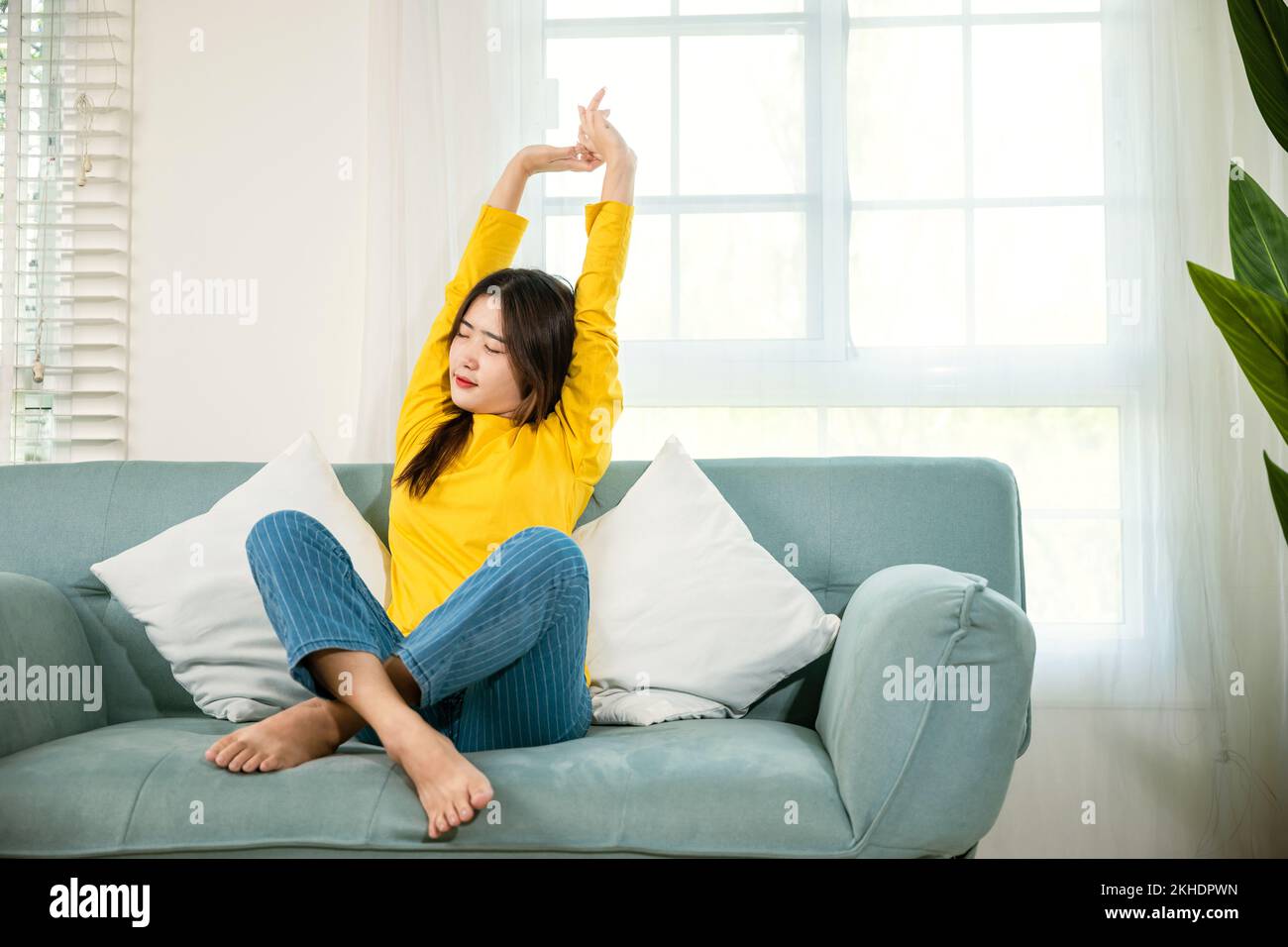 young woman stretching her arms on sofa in the living room at home ...