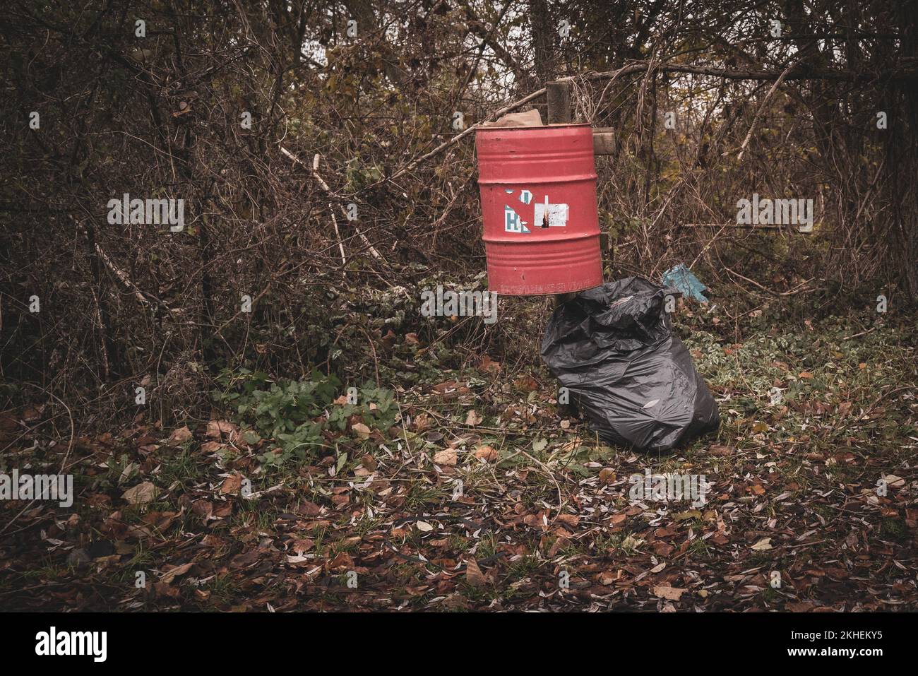 https://c8.alamy.com/comp/2KHEKY5/in-a-parking-lot-there-is-a-red-trash-can-with-a-full-trash-bag-next-to-it-2KHEKY5.jpg