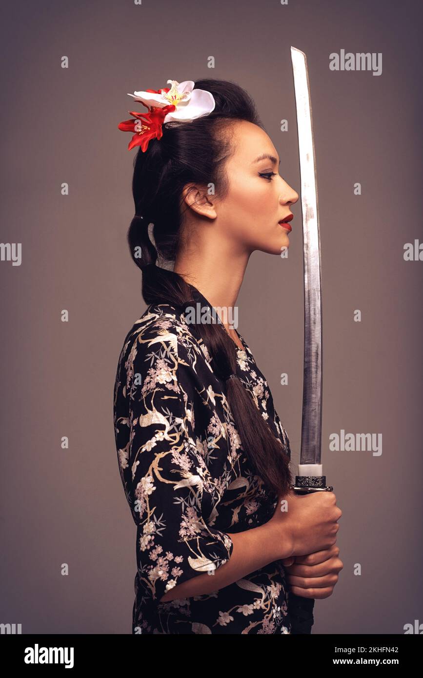 She has great swordsmanship. Studio shot of an attractive young woman holding a samurai sword. Stock Photo