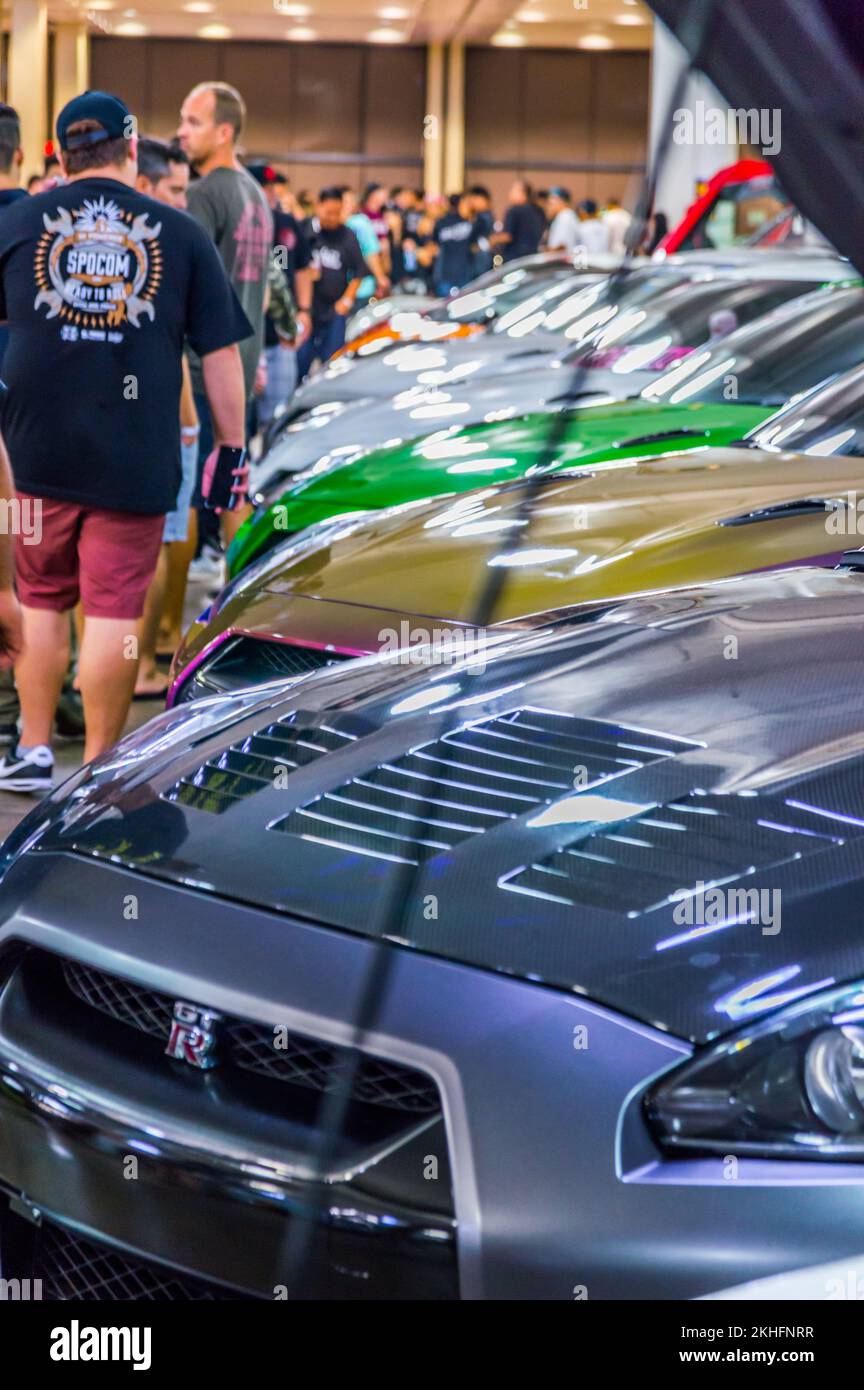 A vertical of crowd looking at cars in a row with open hoods at Hot ...