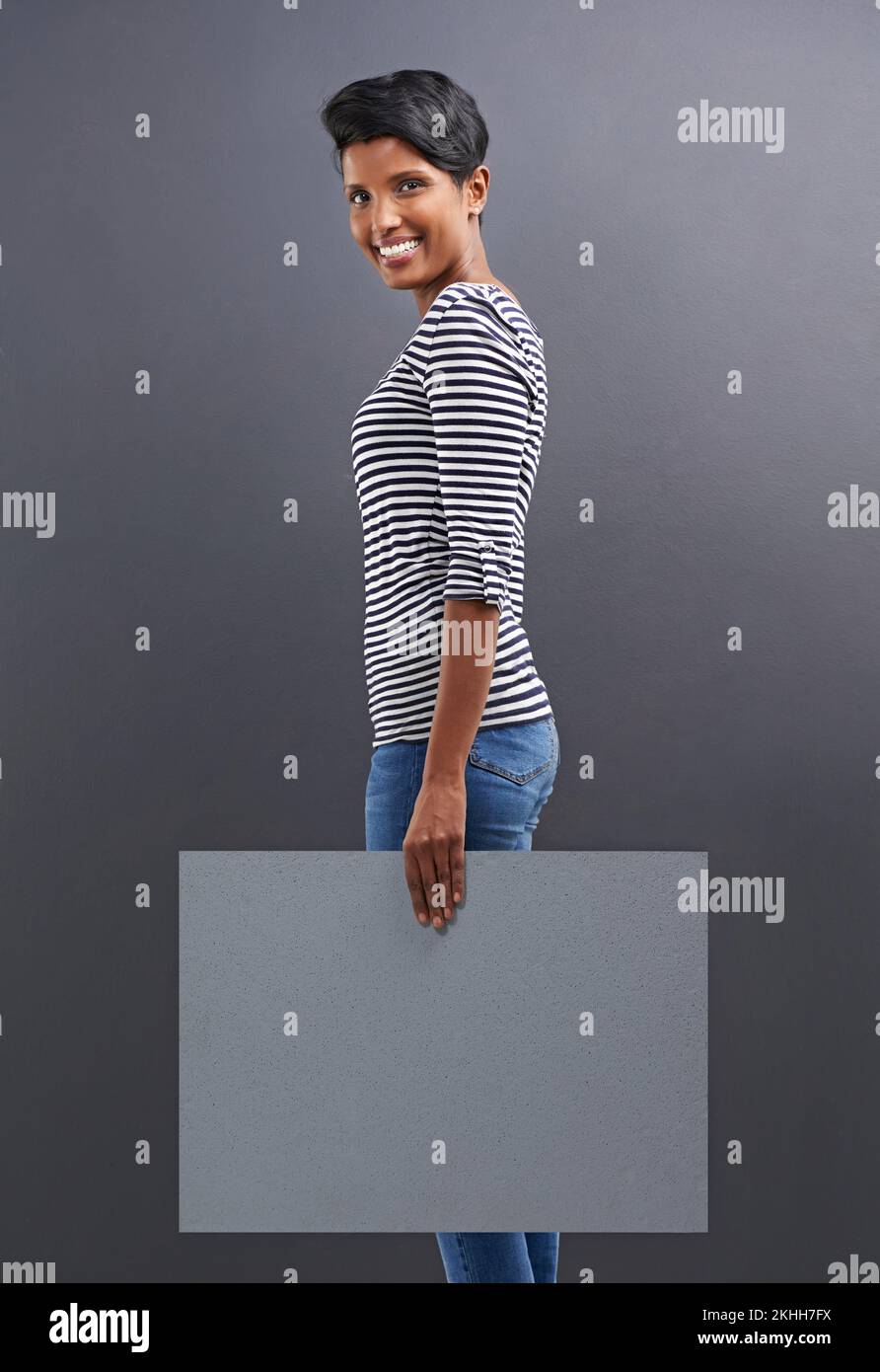 Your copyspace is in safe hands. Studio shot of a beautiful young woman holding a blank placard against a grey background. Stock Photo