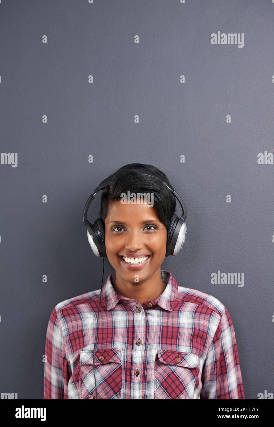 Music and style. Studio shot of a beautiful young woman wearing headphones against a grey background. Stock Photo