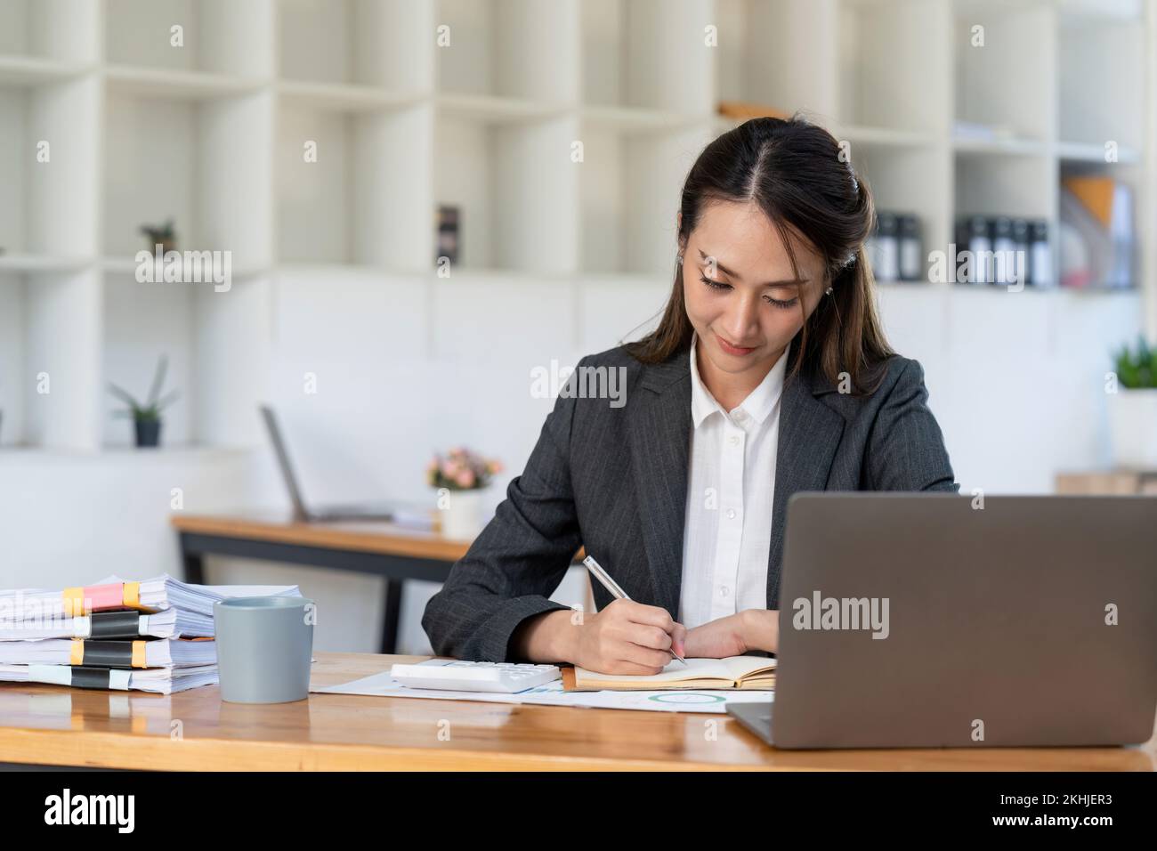 Asian accountant using calculator while taking notes on office desk. Stock Photo