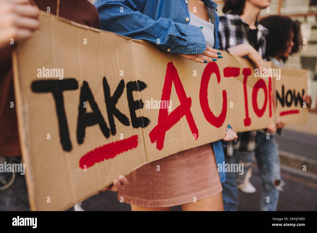 Unrecognizable young people holding a banner while marching against climate change in the city. Multicultural youth activists campaigning for climate Stock Photo