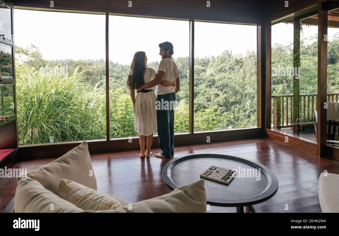 Rear view of loving couple in luxury resort room standing near a window. Man and woman on enjoying holiday. Stock Photo