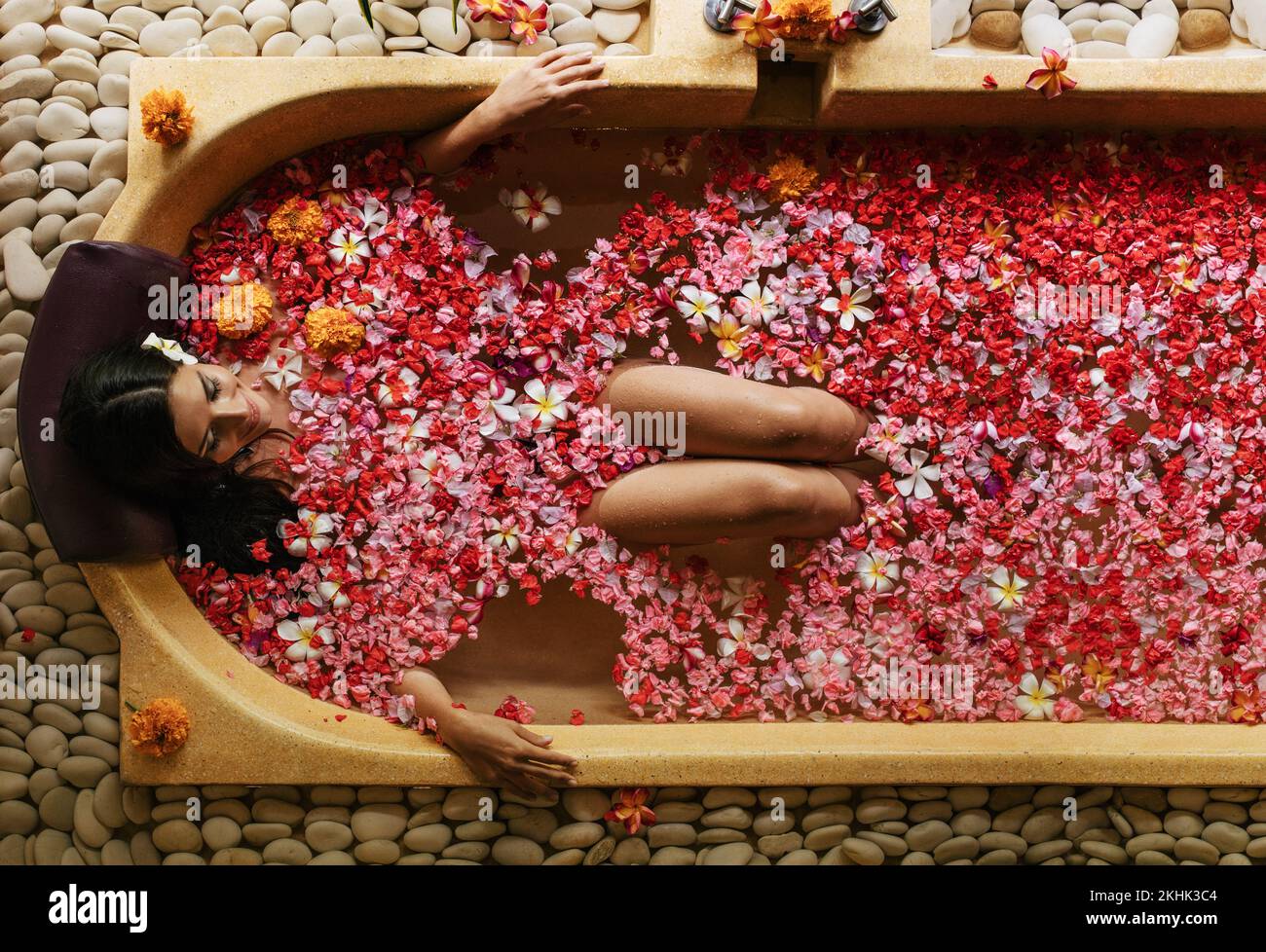 Top view of young woman lying in bath tub with flower petals. Female having flower bath at health spa. Stock Photo