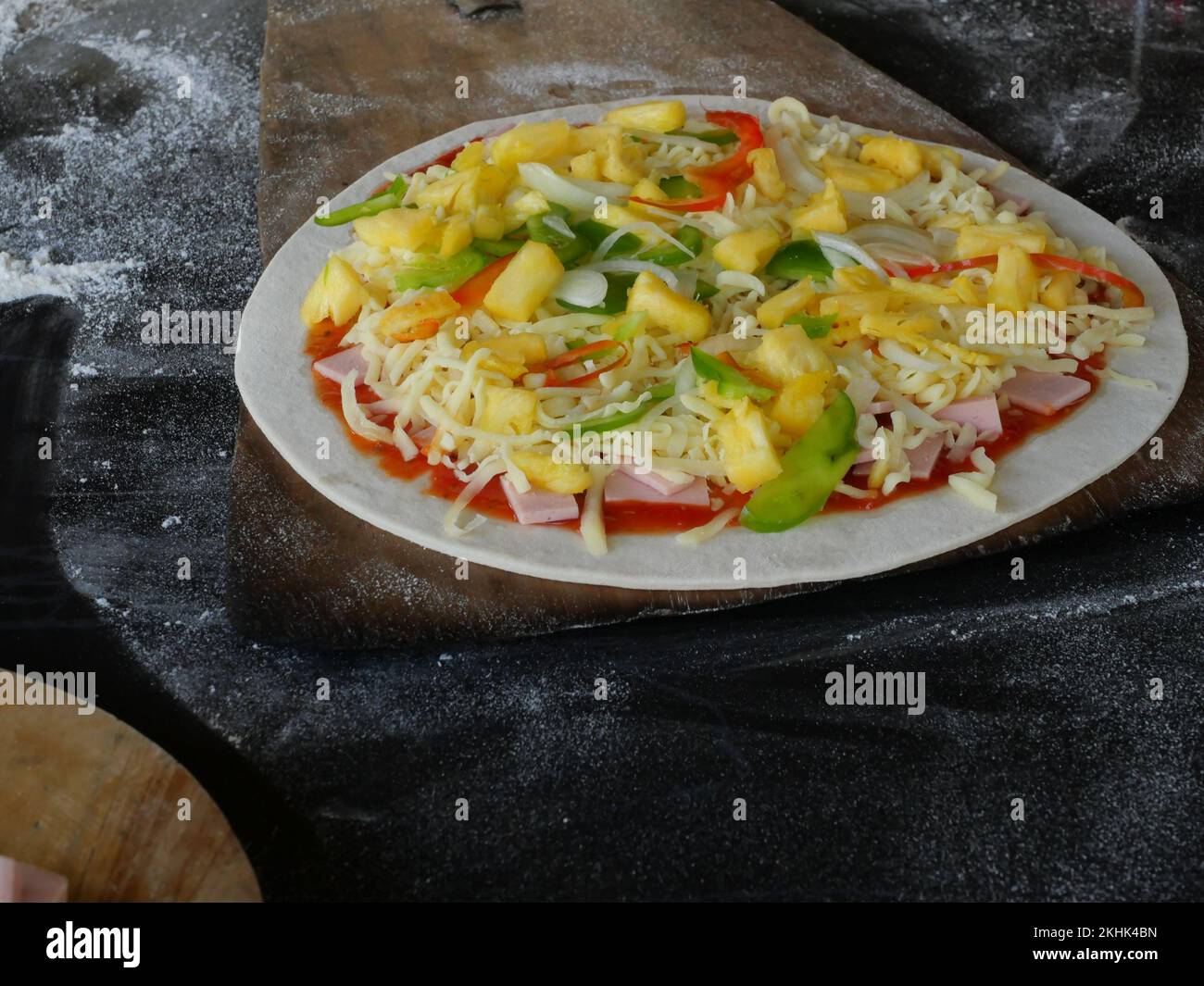 Slices of ham with mozzarella cheese with pineapple and sweet or bell pepper on tomato sauce and flat circle pizza dough on wooden tray Stock Photo