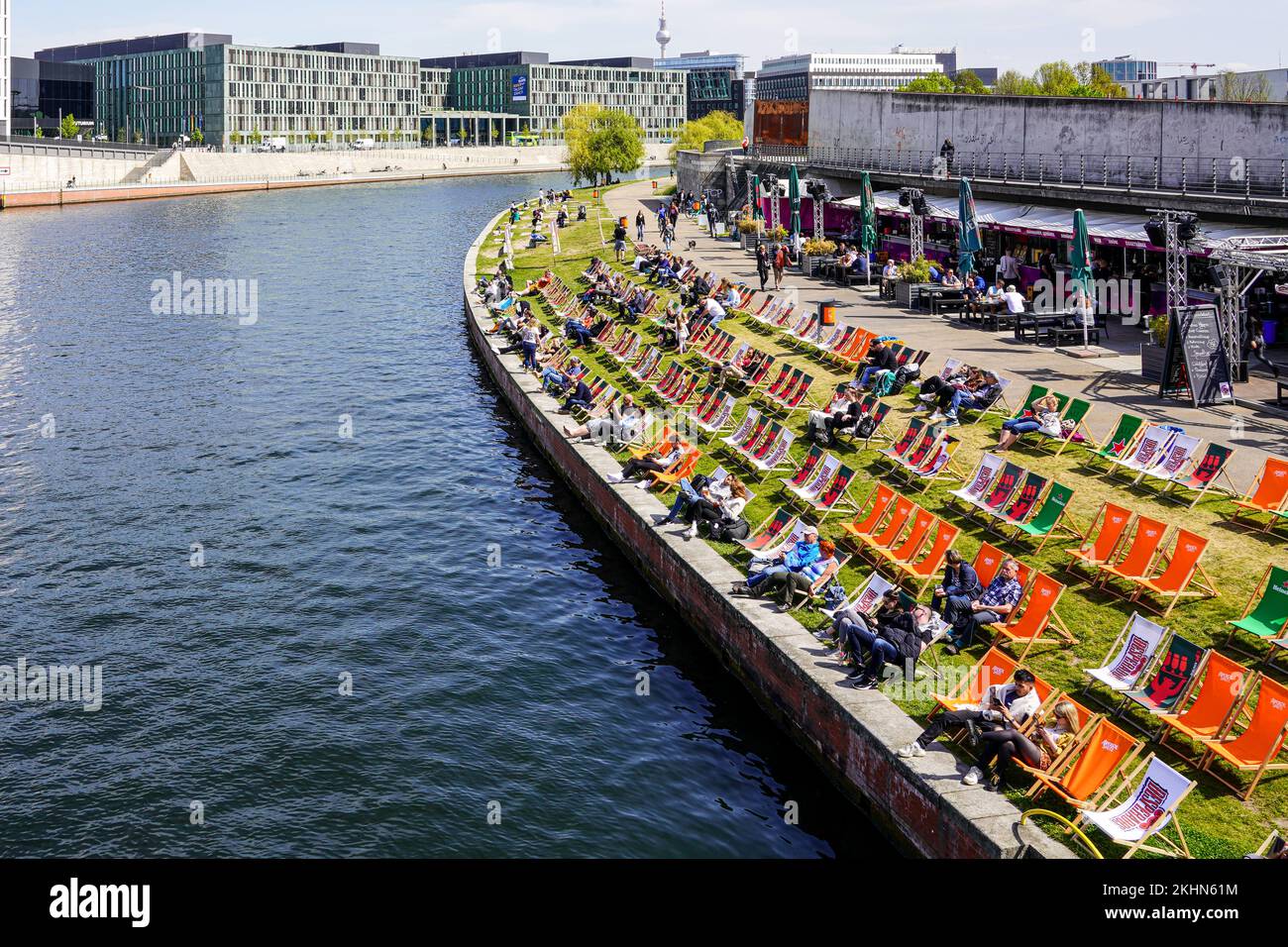 Numerous sun loungers are set up on the banks of the Spree. People enjoy the sunshine in the centre of Berlin opposite the main railway station. Stock Photo