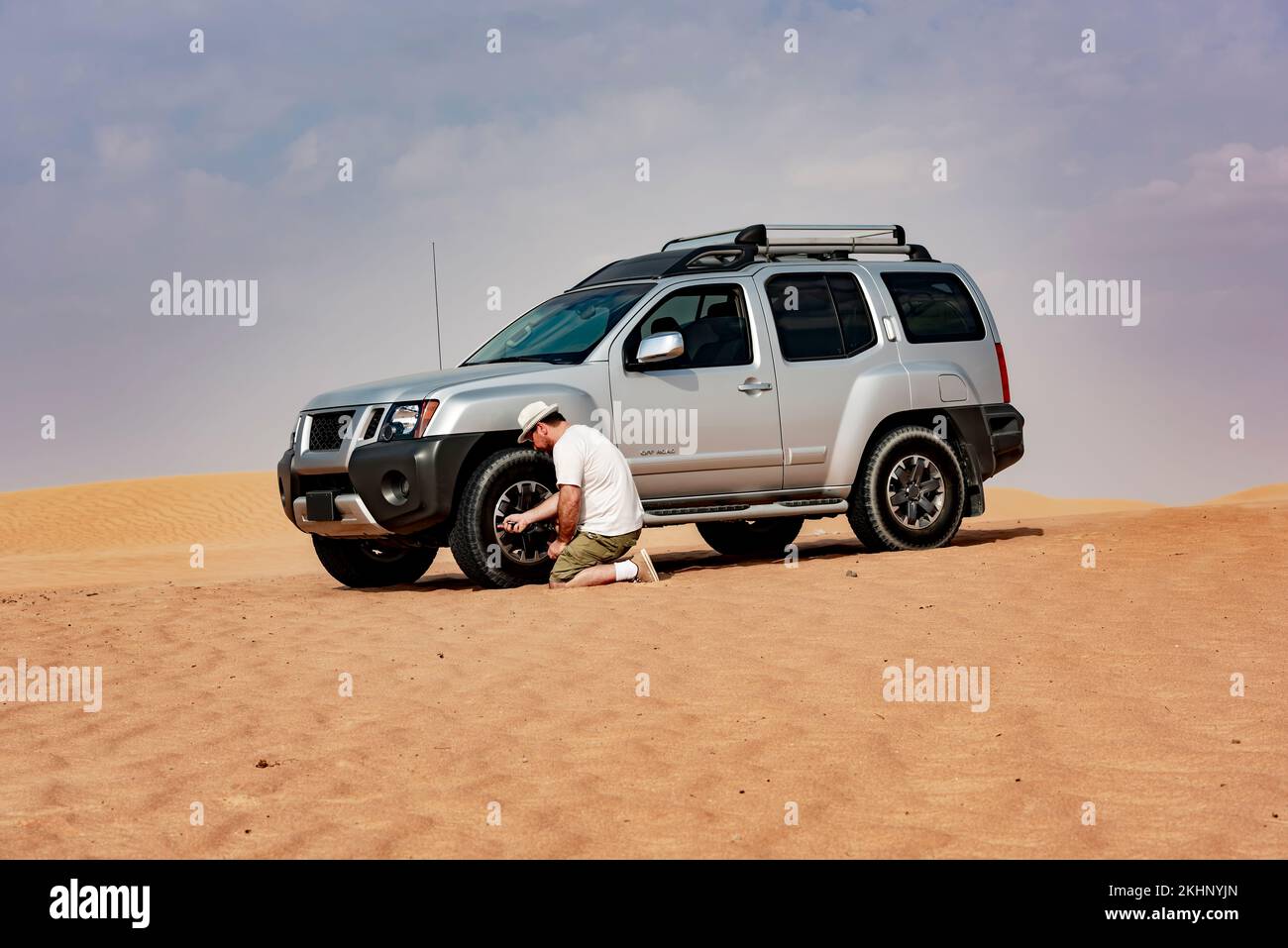 Man deflates tires for safe dune driving in vast desert, off-road adventure Stock Photo
