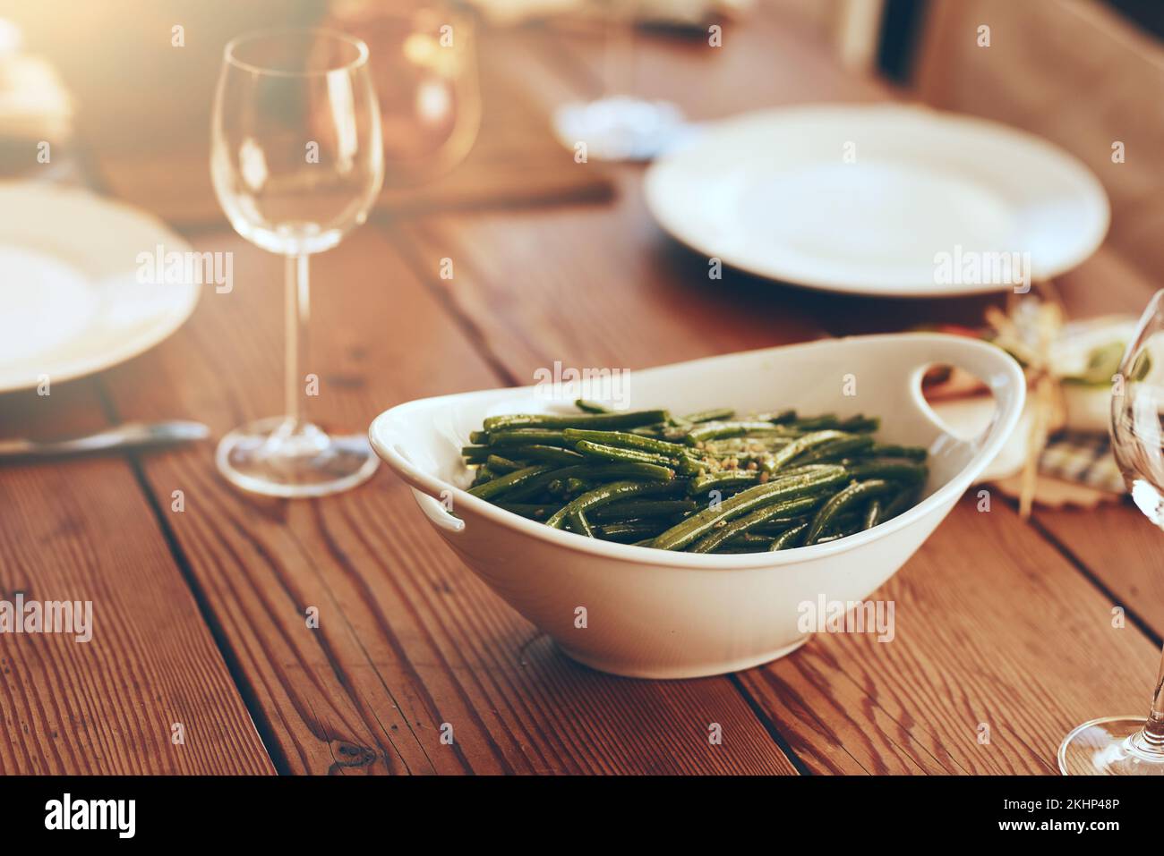Thanksgiving, green beans and food with a place setting on a dining room table for a celebration event. Party, dish and dinner with a bowl on a wooden Stock Photo