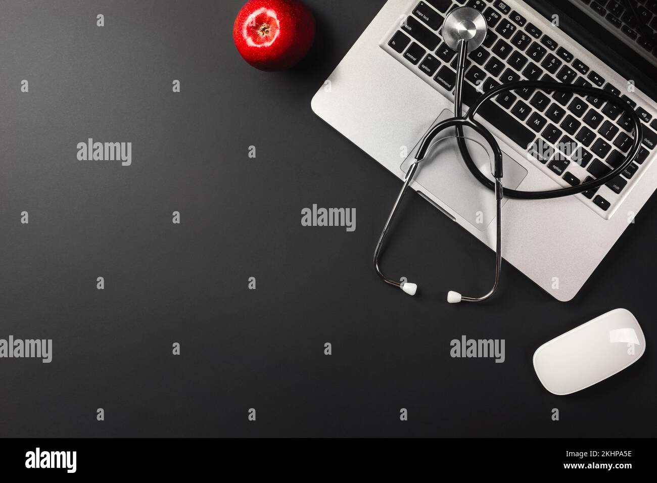 Laptop on a black desktop with a red apple on the table and a stethoscope for a doctor working on social networks. View from above. High quality photo Stock Photo