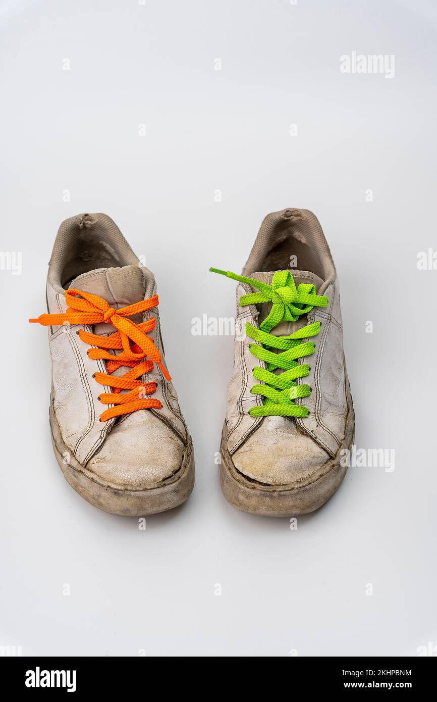 worn old torn white sneakers with colored laces on a white background ...