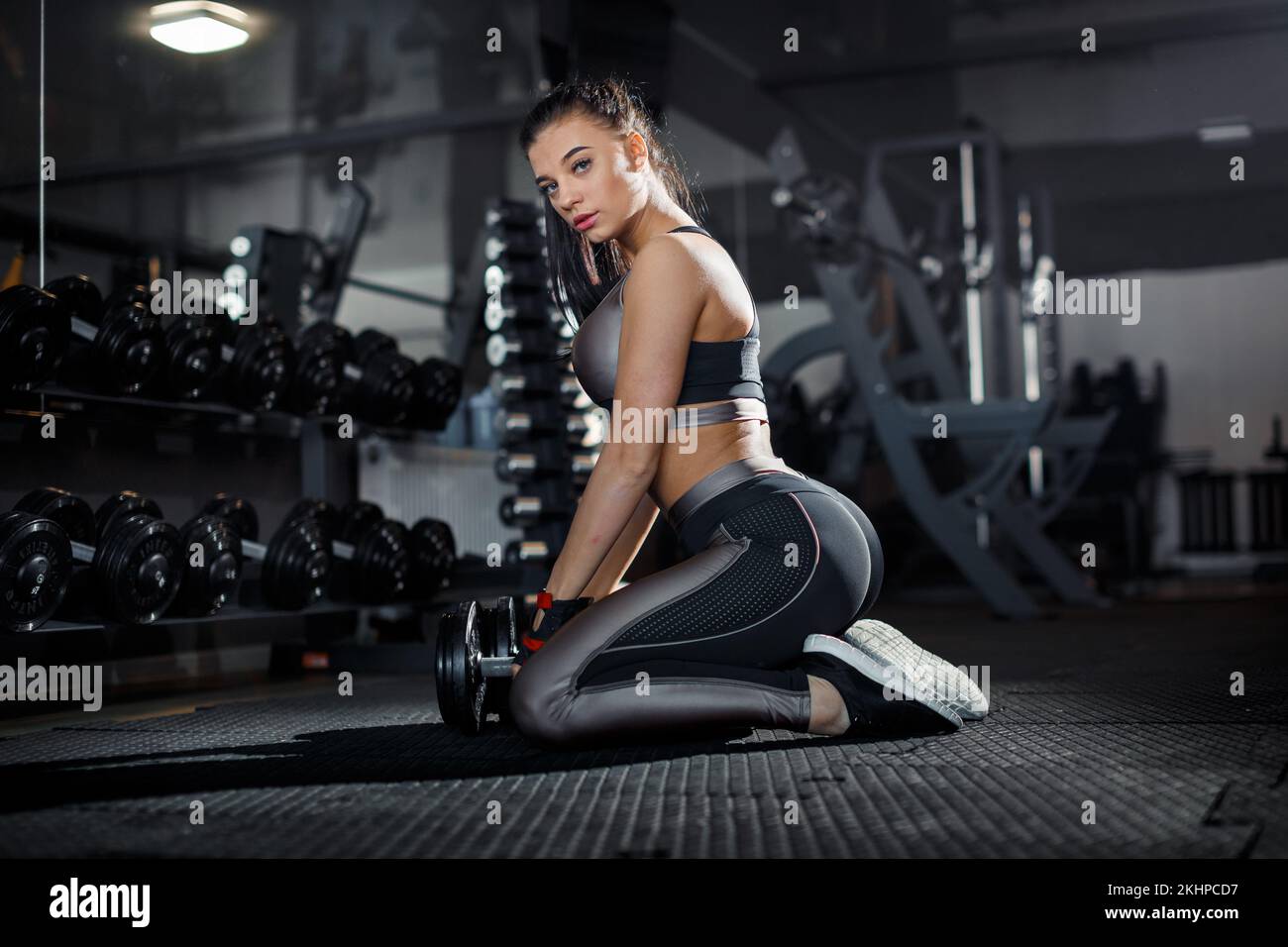 Slim, bodybuilder girl, lifts heavy dumbbell standing in front of the mirror while training in the gym. Sports concept, fat burning and a healthy life Stock Photo