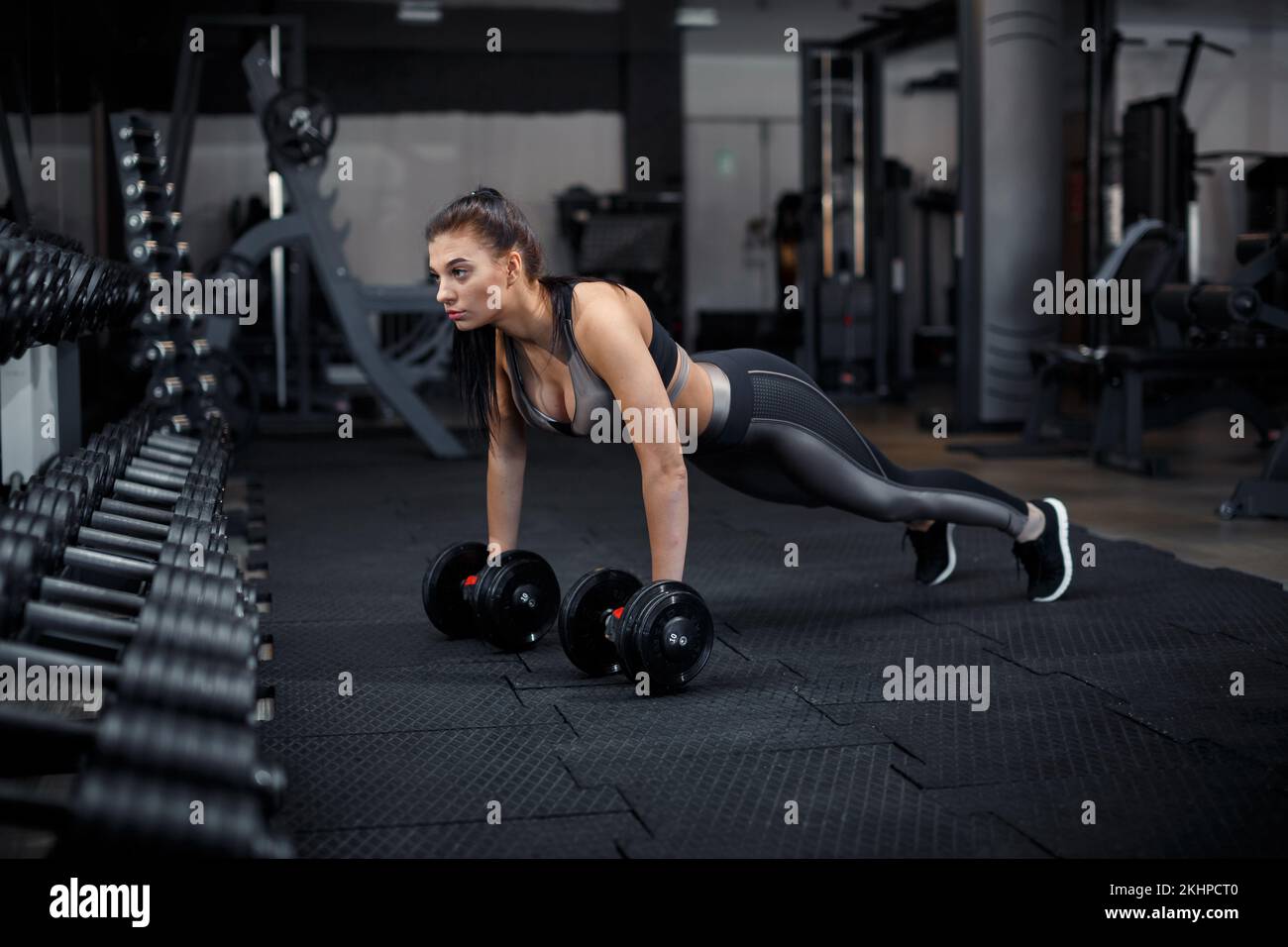 Slim, bodybuilder girl, lifts heavy dumbbell standing in front of the mirror while training in the gym. Sports concept, fat burning and a healthy life Stock Photo