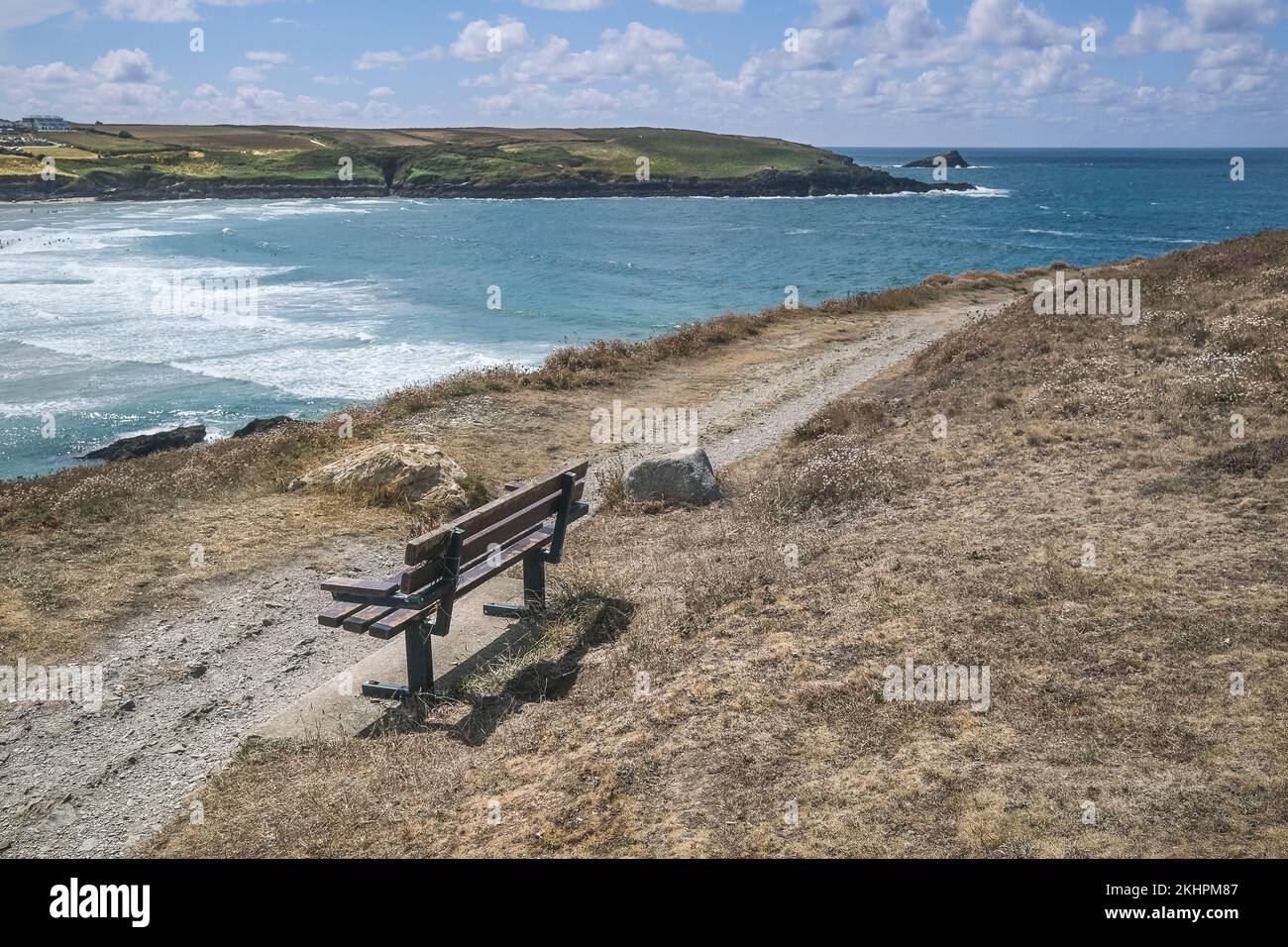 A bench on a rough footpath leading to a view of the rocky island The Goose off coast of Pentire Point East in Newquay in Cornwall in the UK. Stock Photo