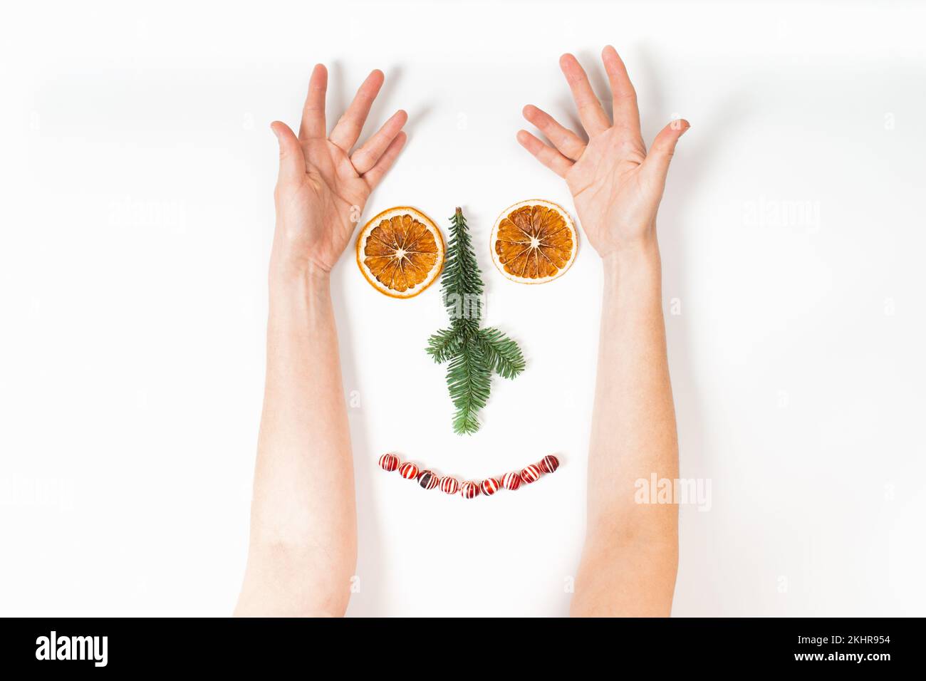 Funny deer face of Woman's hands and Christmas decorations with dry orange, fir tree and candies on white Stock Photo